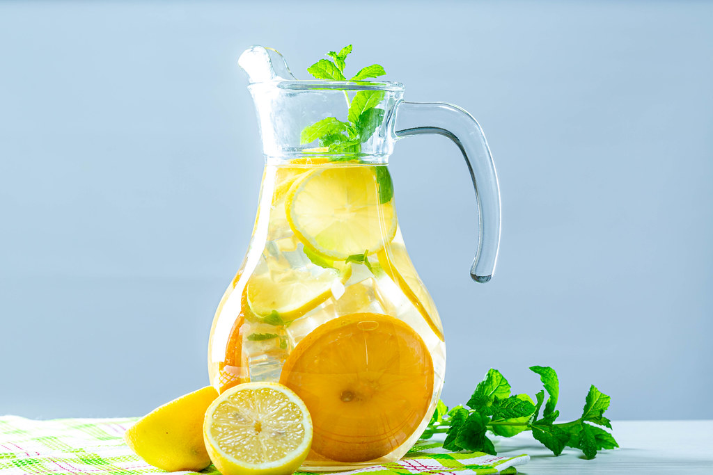 Lemonade pitcher with lemon, mint and ice on table